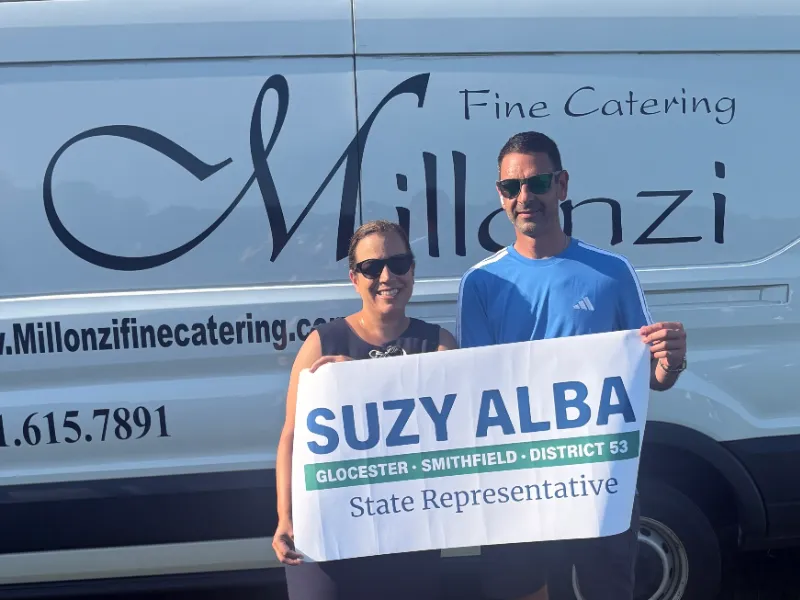 Suzy and a supporter holding a campaign sign in front of a catering van